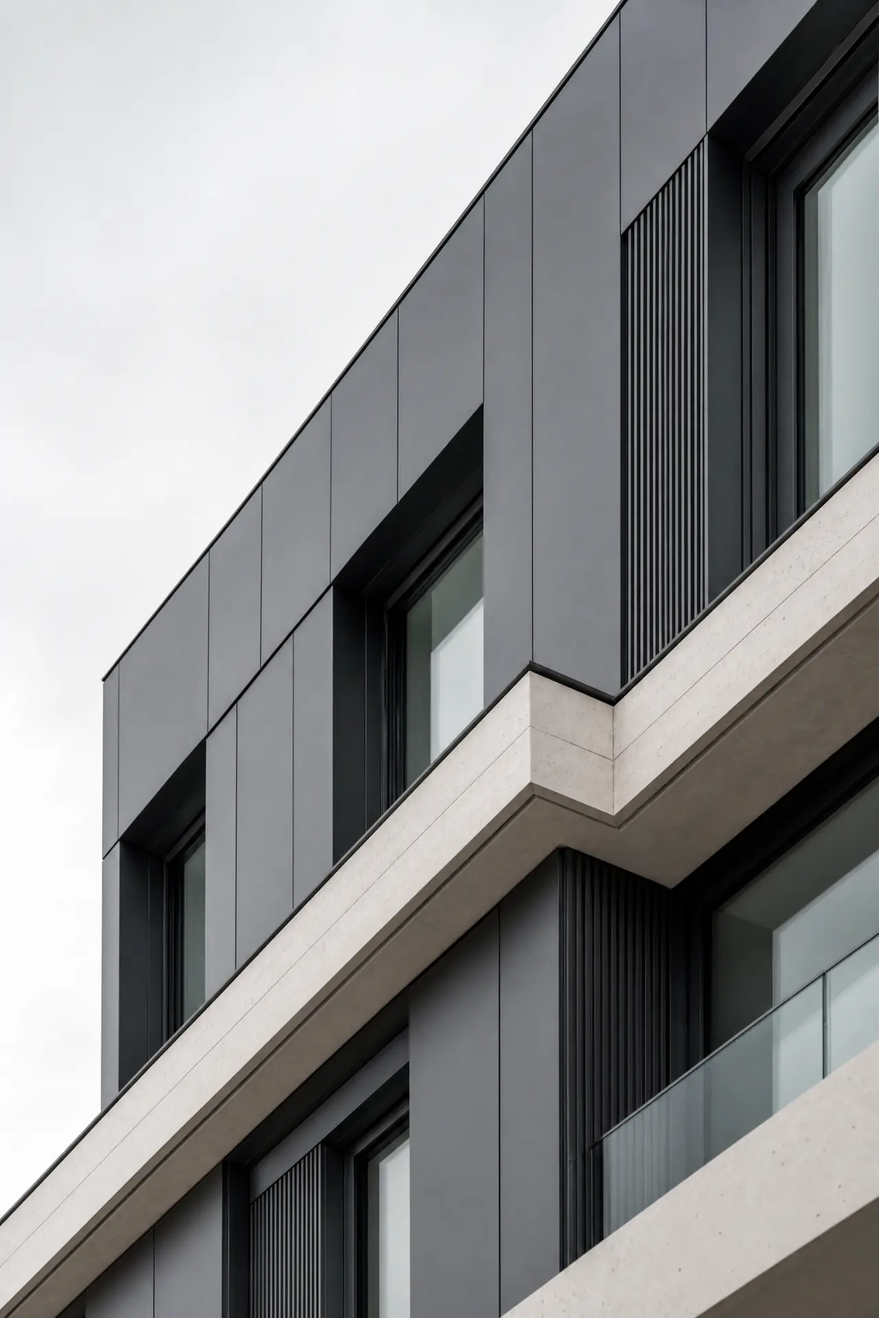 Close-up of a dark metal clad façade corner with stone banding